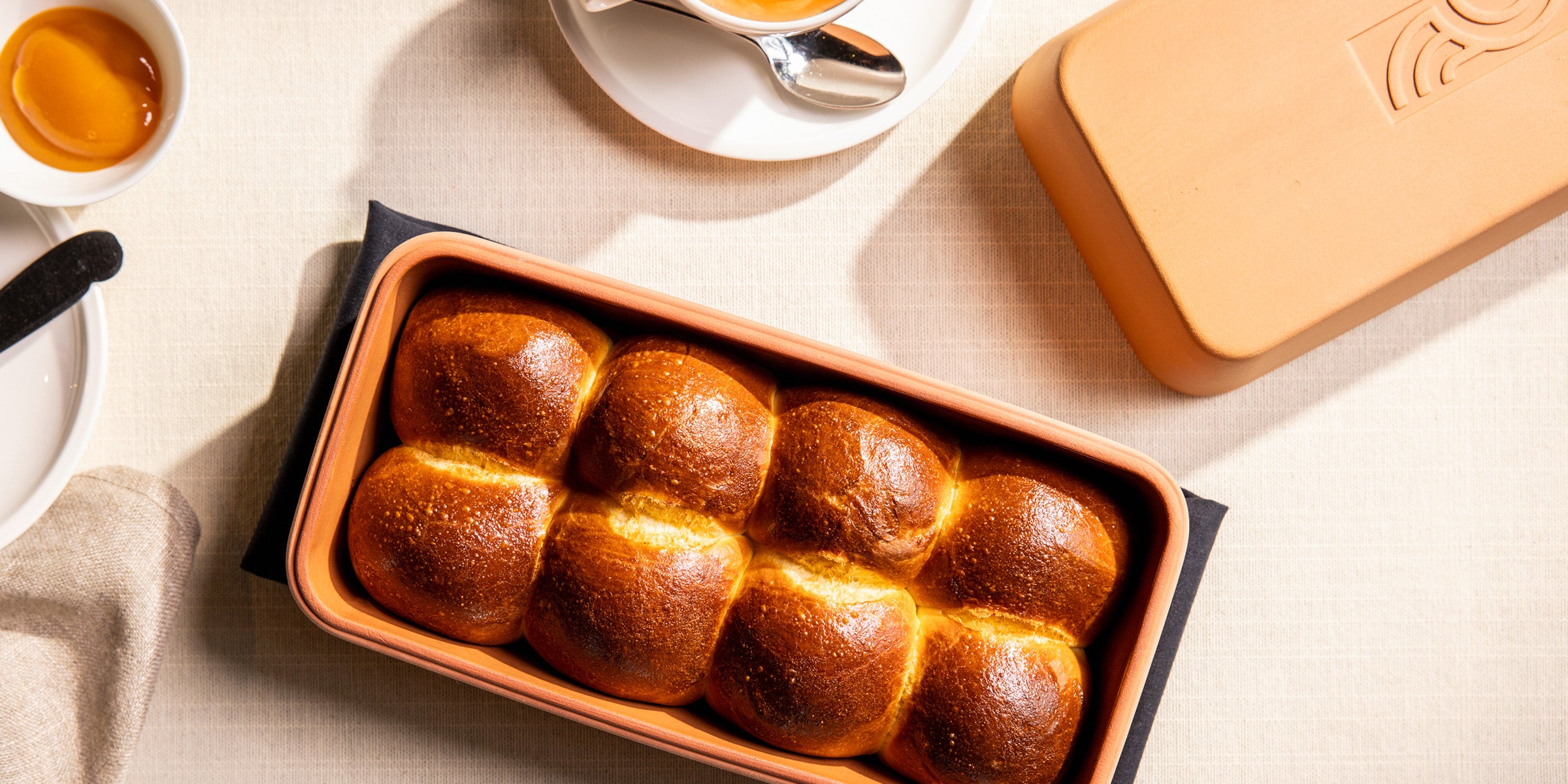 Goldbraune Brioche-Brötchen im myromy Brick Classic Backstein aus Keramik, daneben der passende Deckel aus der Draufsicht