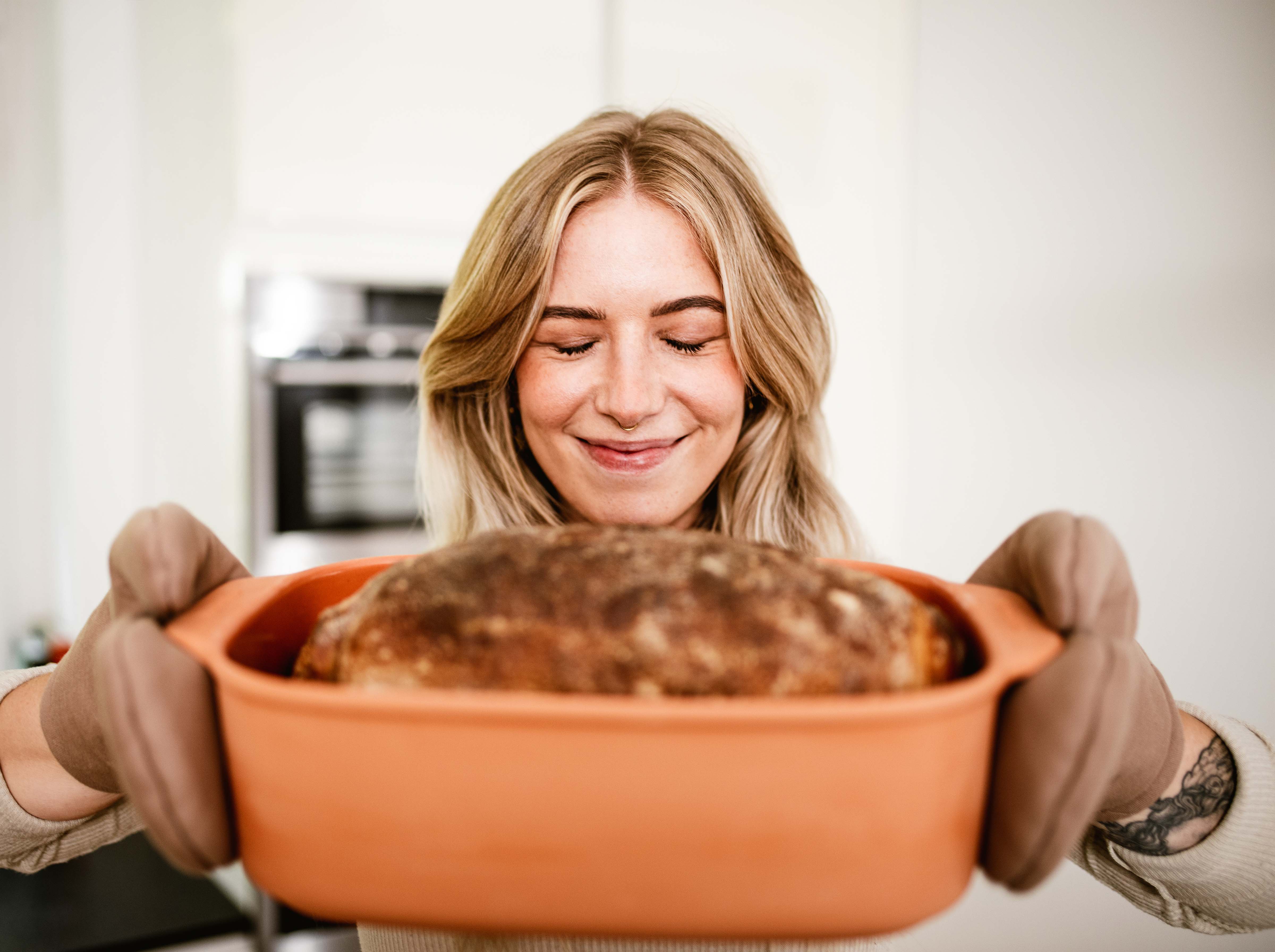 Frau hält frisch gebackenes Brot im myromy Multi-Bräter als Keramik-Brotbackform und Brottopf mit Ofenhandschuhen