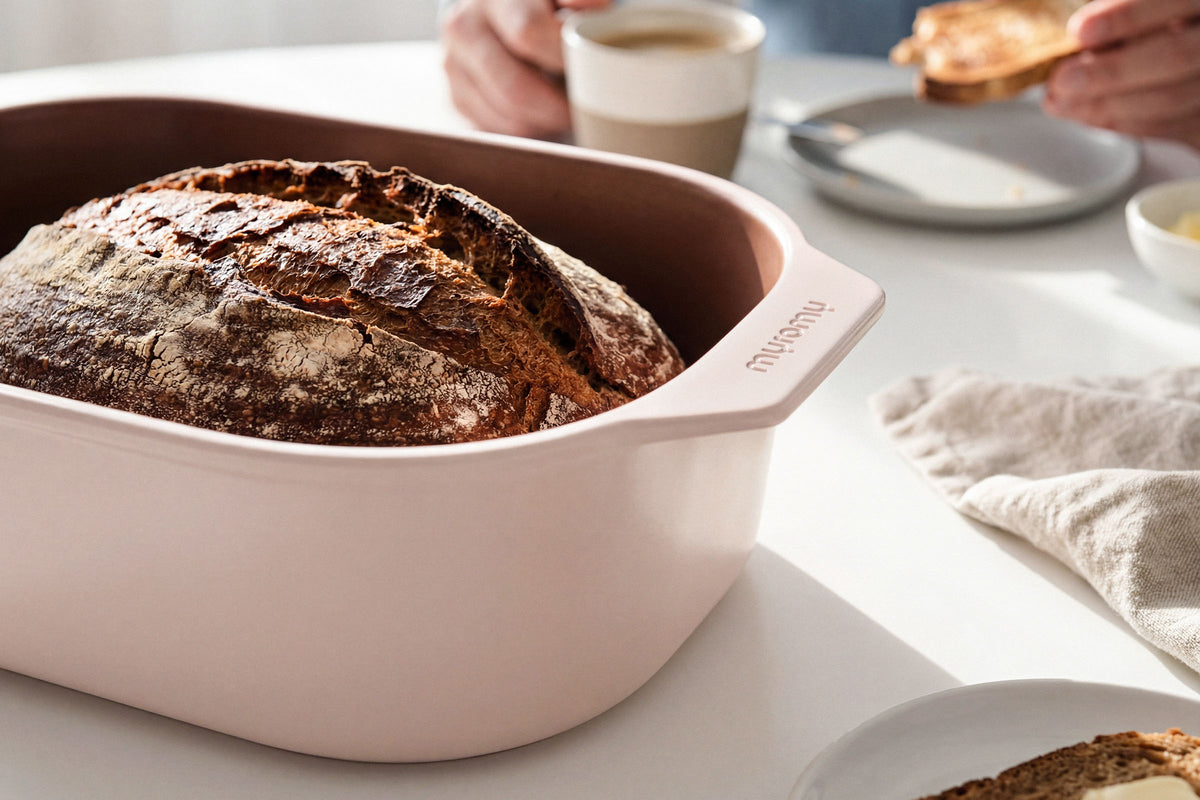 Frisch gebackenes Sauerteigbrot im weißen myromy Multi-Bräter als Keramik-Brotbackform und Brottopf auf dem Frühstückstisch