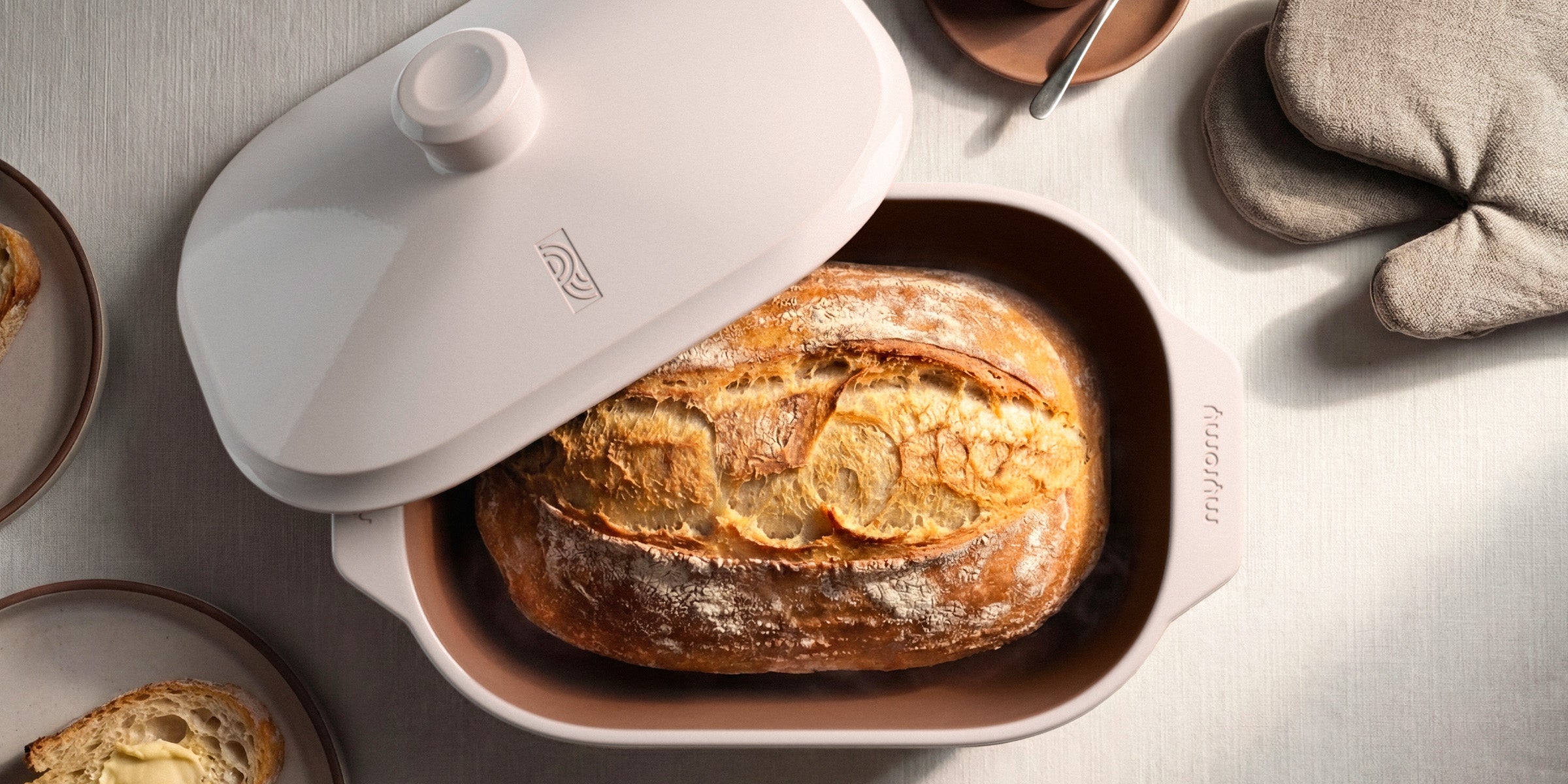 Frisch gebackenes Sauerteigbrot im weißen myromy Multi-Bräter als Keramik-Brotbackform, mit aufgelegtem Deckel aus der Draufsicht