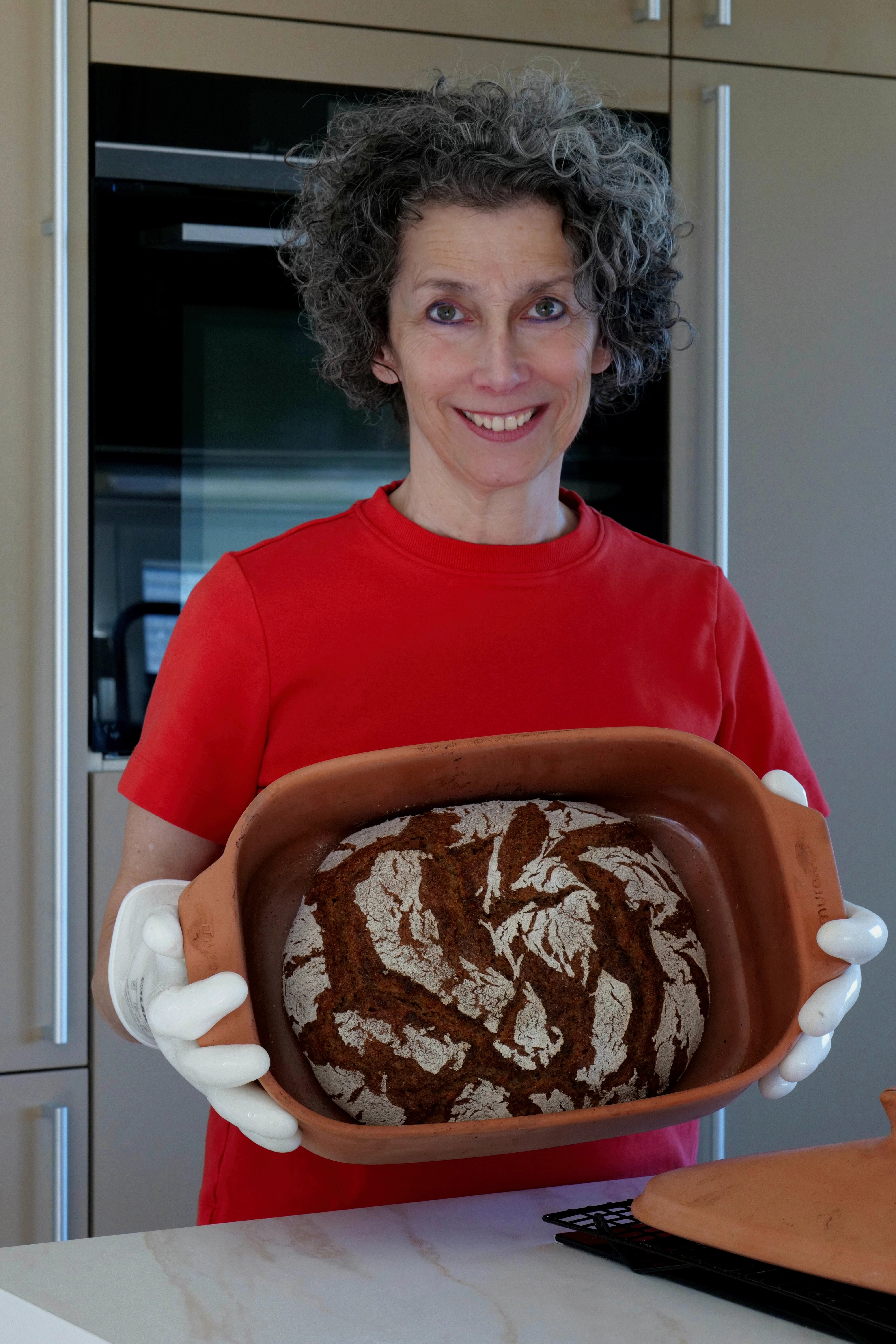 Eine Frau posiert mit frischem Brot im myromy Brotbackform aus Ton in terracotta