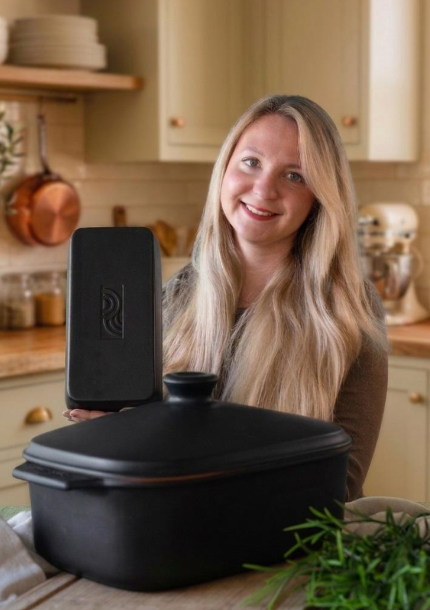 Frau präsentiert einen schwarzen myromy Brick aus Keramik, davor steht ein schwarzer myromy Multi-Bräter mit Deckel in einer Küche