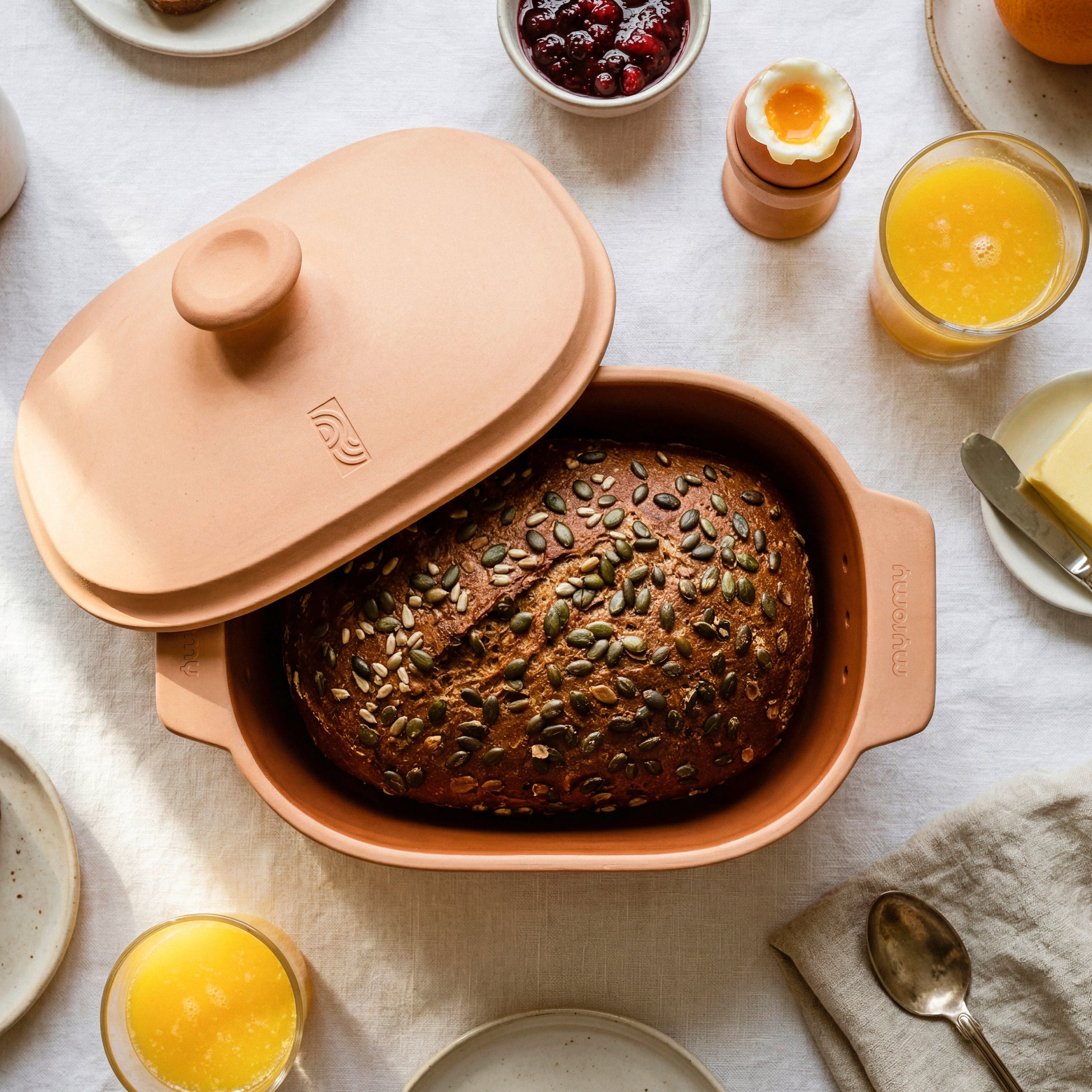 Frisch gebackenes Körnerbrot im geöffneten myromy Brot-Frische-Topf Medium auf einem gedeckten Frühstückstisch
