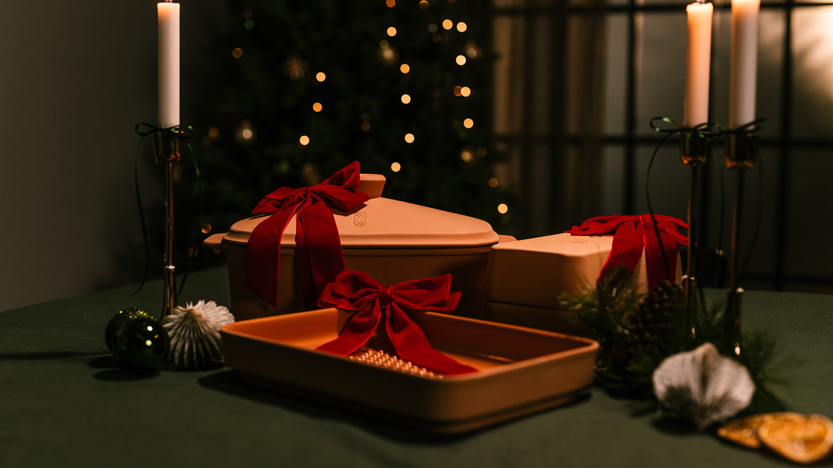 Festlich dekoriertes myromy Kochgeschirr aus Keramik mit Schmortopf, Keramik-Grillplatte und Backstein als Weihnachtsgeschenke mit roten Schleifen