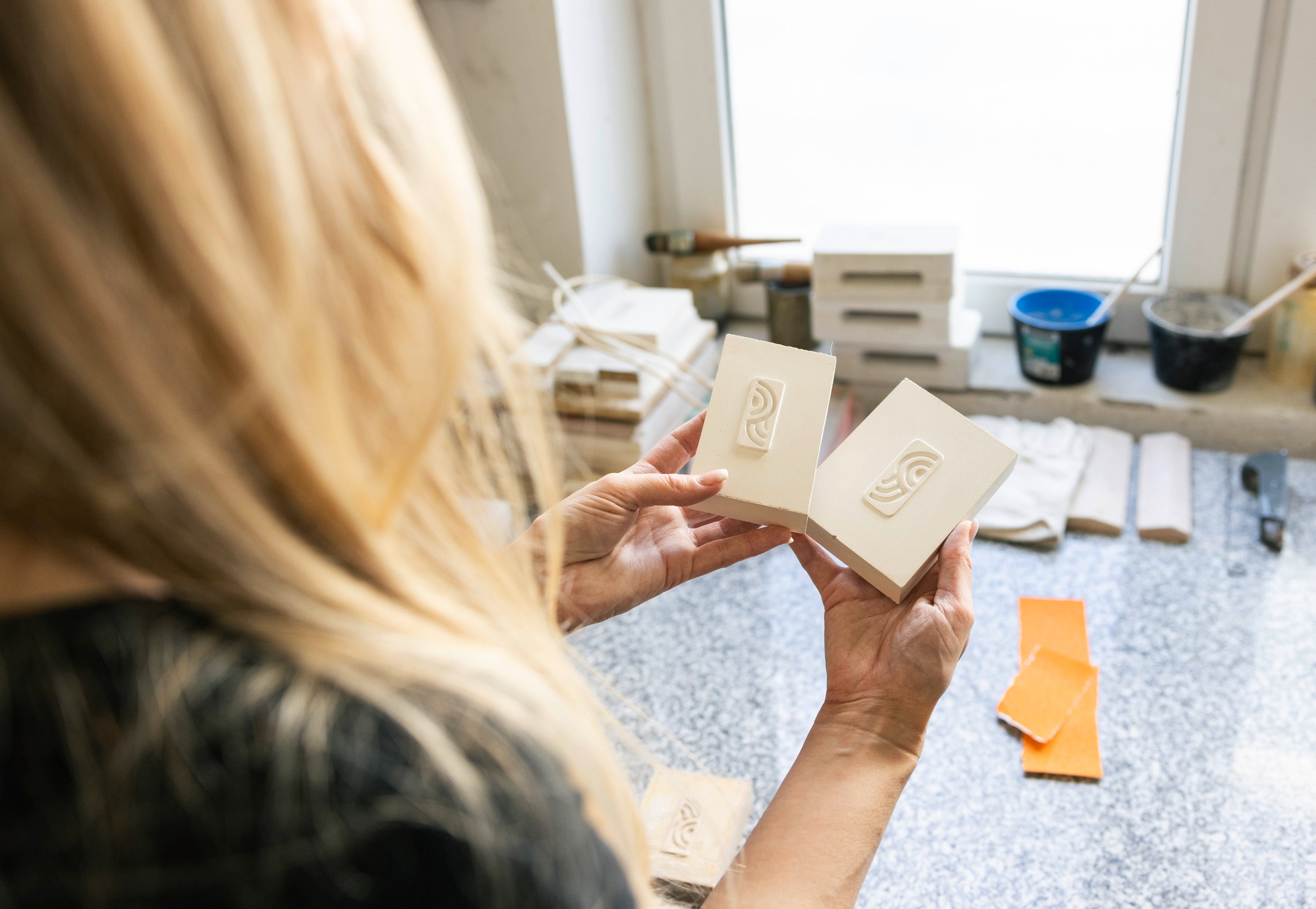 Mitarbeiterin hält zwei myromy Logo-Prägungen aus Keramik während der handwerklichen Qualitätskontrolle in der Manufaktur
