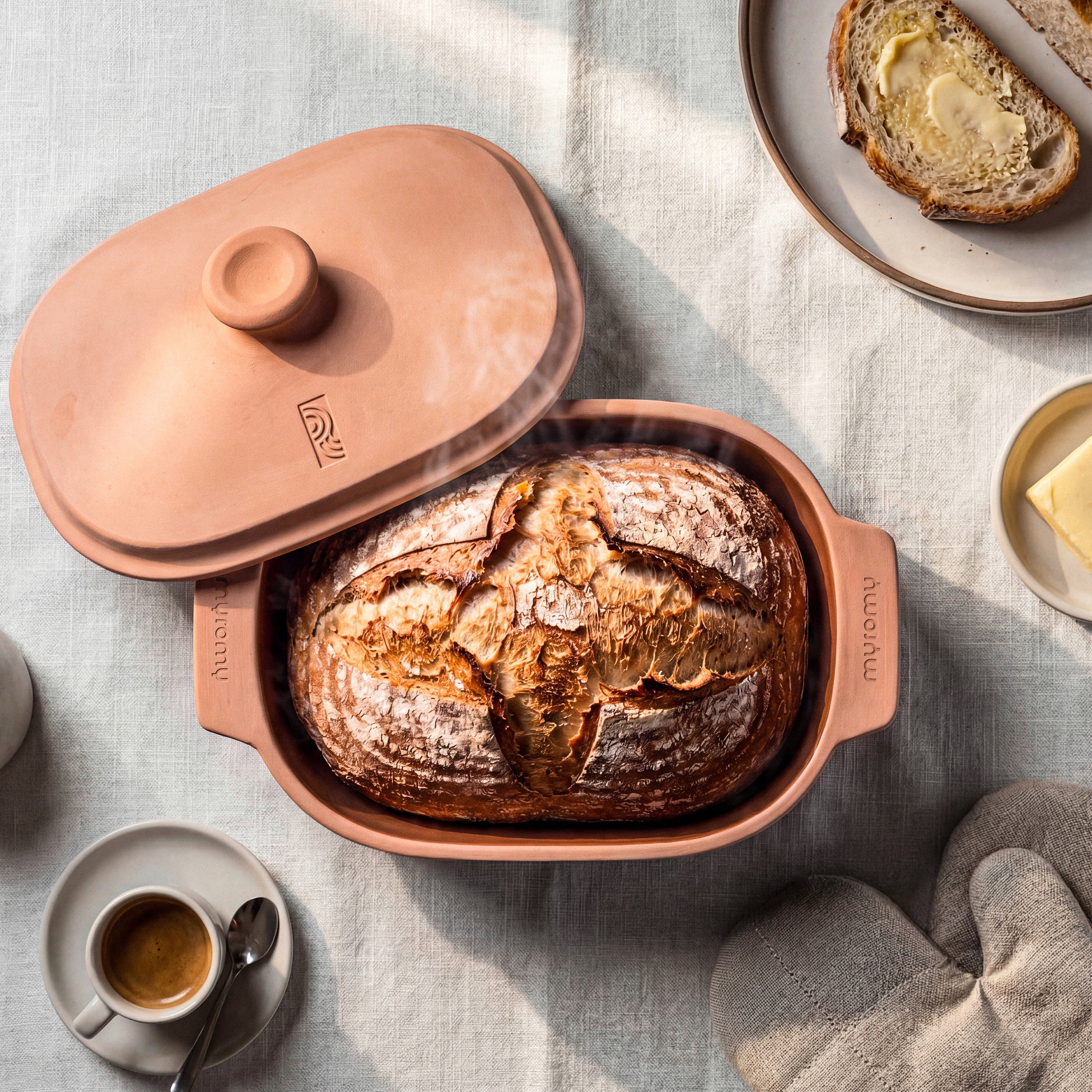 Frisch gebackenes Brot im geöffneten myromy Multi-Bräter und der Brotbackform 3,5 L Medium in der Signature Edition, daneben Butter und Kaffee
