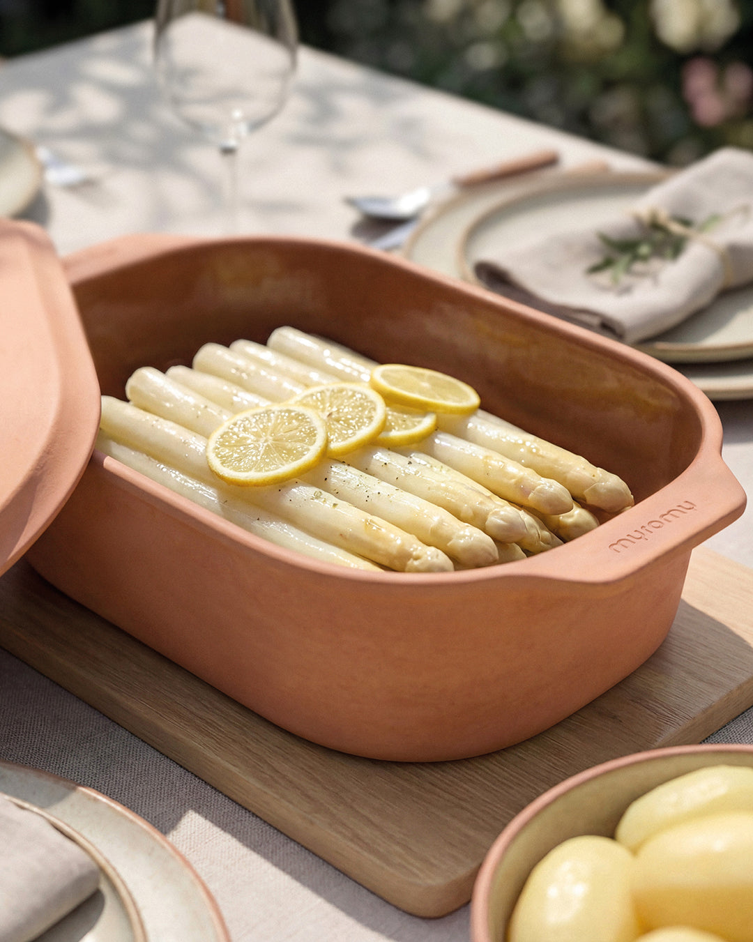 Weißer Spargel mit Zitronenscheiben im geöffneten myromy Multi-Bräter und der Brotbackform in der Signature Edition auf einem gedeckten Tisch